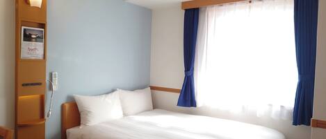 Une chambre d’hôtel avec un lit, une table de chevet, une lampe fixée au mur et une fenêtre avec des rideaux.
