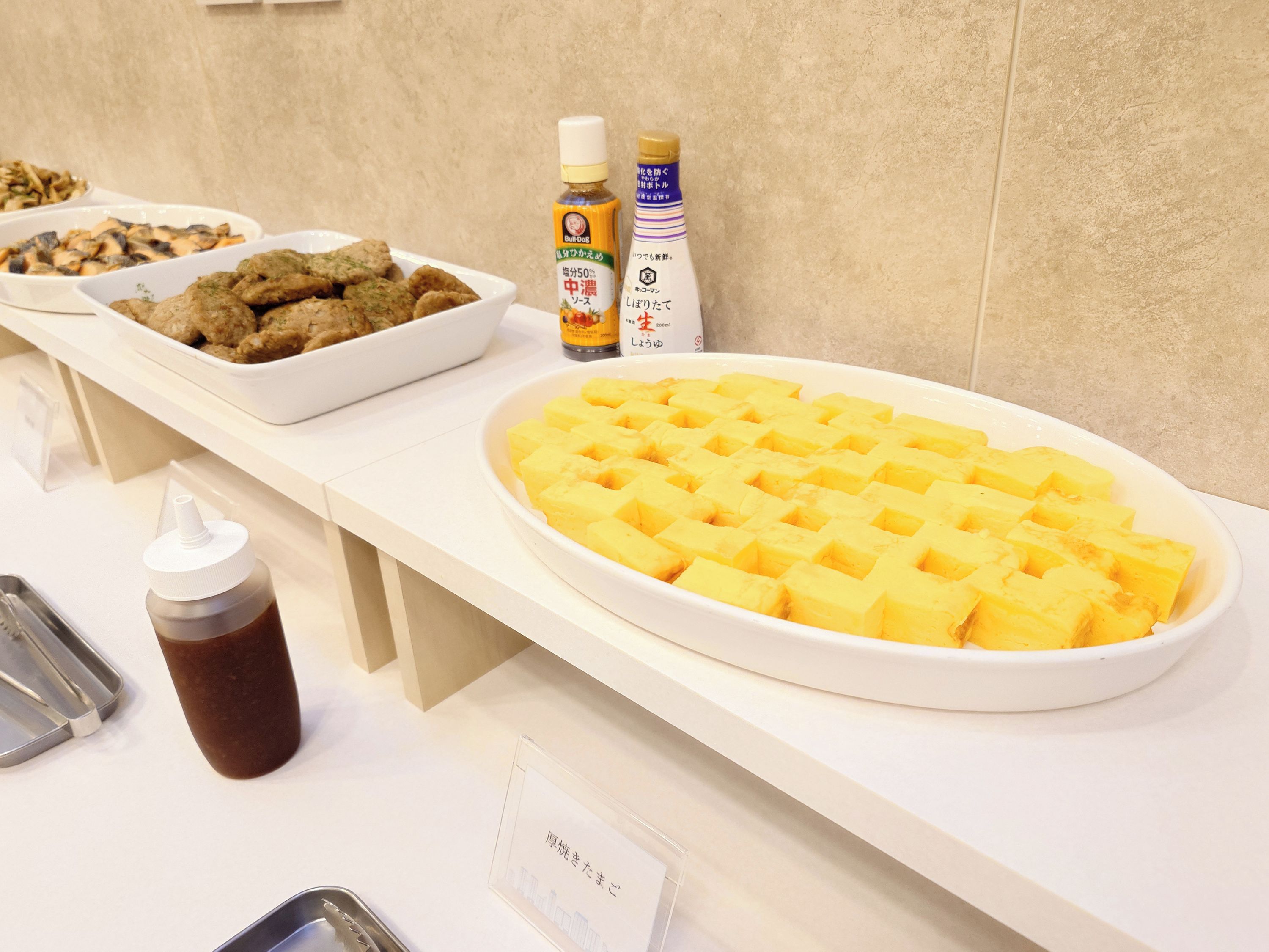 A buffet table with various food items including waffles, meatballs, and a bottle of sauce.