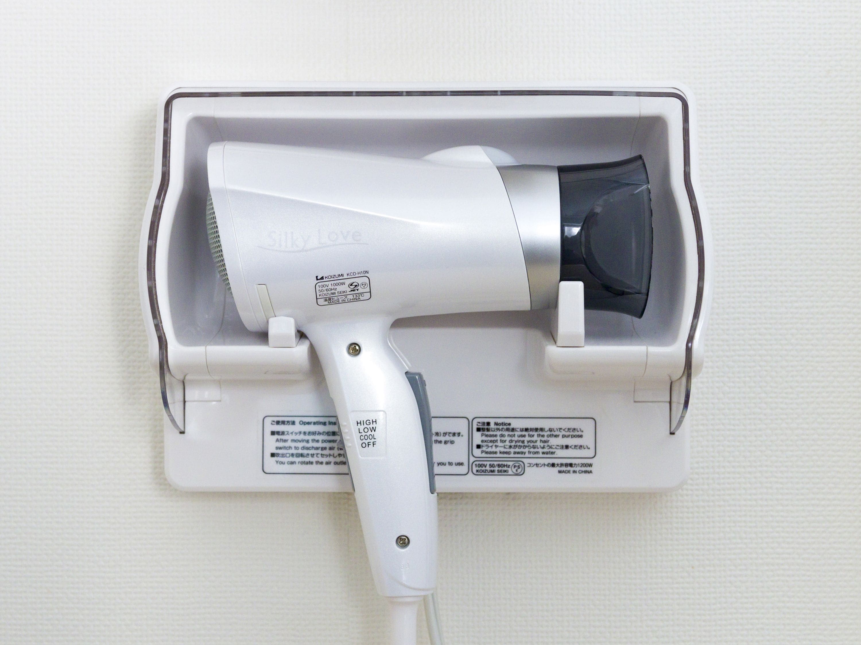A hair dryer mounted on a wall with a power cord plugged in.