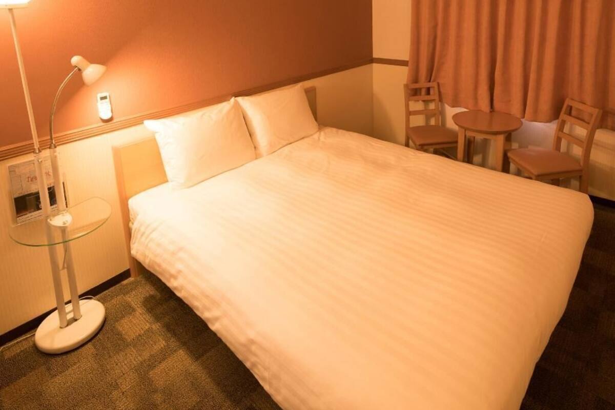 Ein Hotelzimmer mit einem großen Bett, Nachttisch, Lampe und zwei Stühlen.