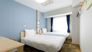 Ein Hotelzimmer mit zwei Betten, einem Schreibtisch, einem Stuhl, einem Kleiderschrank und einem fenster mit Vorhängen.