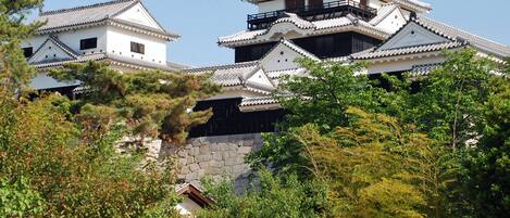 A traditional Japanese castle with multiple white buildings, stone walls, and surrounding greenery.