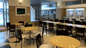 A modern cafe with multiple tables and chairs, vending machines, and a large window offering a view of the city. - Toyoko Inn Kagoshima Temmonkan No.1 (Kagoshima)