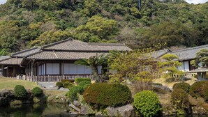 Traditional Japanese-style buildings with a pond in the foreground and a forested hill in the background. - Toyoko Inn Kagoshima Temmonkan No.1 (Kagoshima)