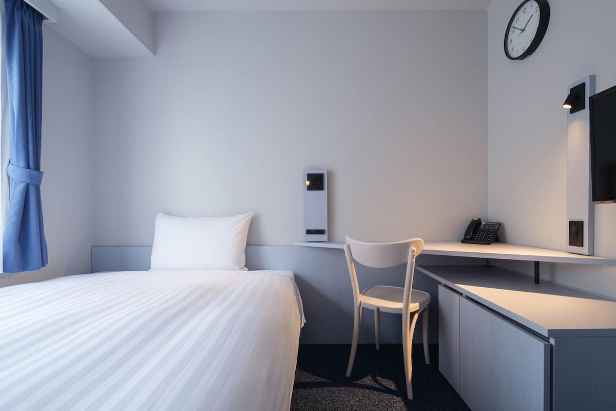 Une chambre d’hôtel comprenant un lit, un bureau avec une chaise, une horloge et un téléphone.