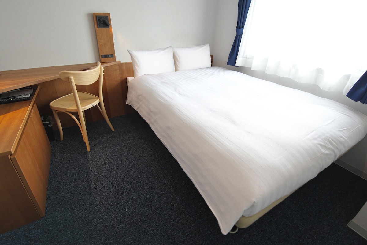 Une chambre d’hôtel avec un lit, un bureau, une chaise et une fenêtre avec des rideaux.