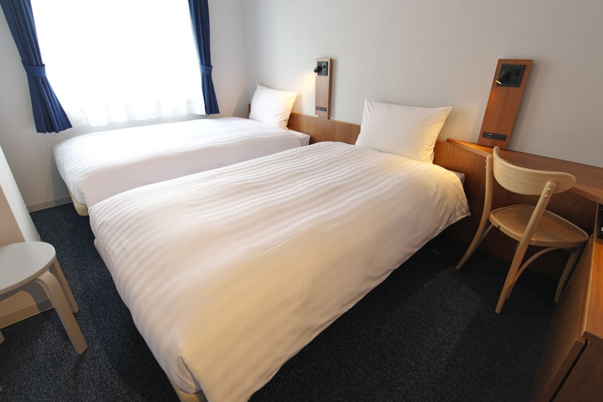 Une chambre d’hôtel avec deux lits, un bureau, une chaise et une table de chevet.
