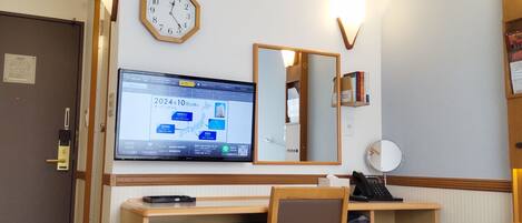 Ett hotellrum med ett skrivbord, en stol, en luftkonditioneringsanläggning, en klocka och en tv som visar en karta.