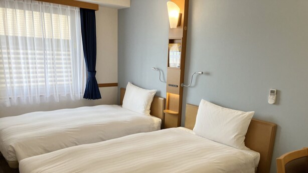 A hotel room with two beds, a window with sheer curtains, a bedside table, and a wall-mounted light fixture. - Toyoko Inn Fukushima-eki Higashi-guchi No.1 (Fukushima)