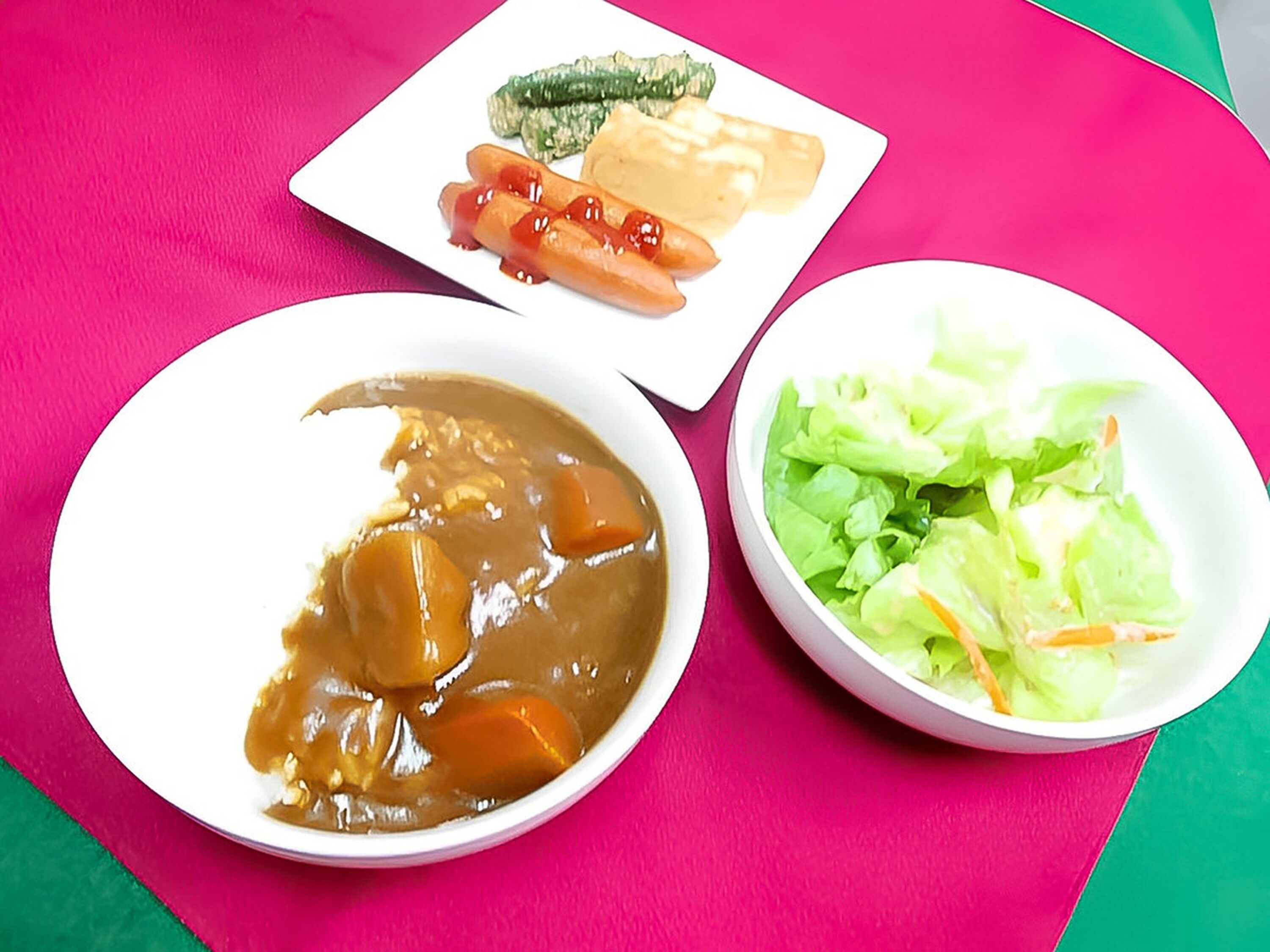 A plate with a bowl of soup, a plate with vegetables, and a plate with a hot dog.