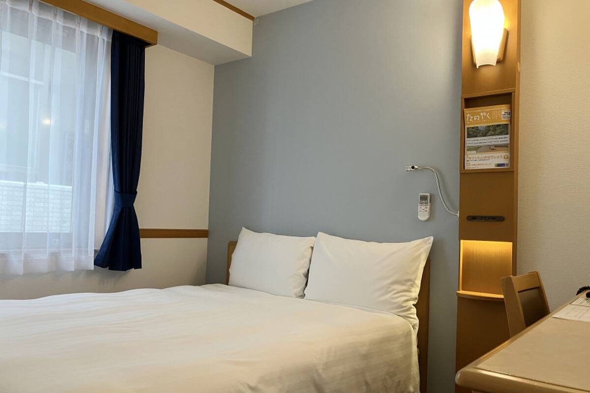 Een hotelkamer met een bed, een bureau, een stoel, een raam met gordijnen en een wandlamp.
