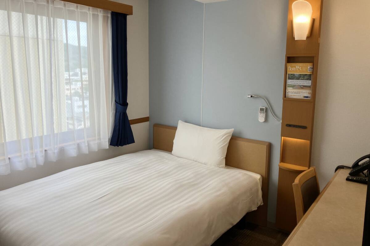 Een hotelkamer met een bed, een bureau, een telefoon en een wandlamp.