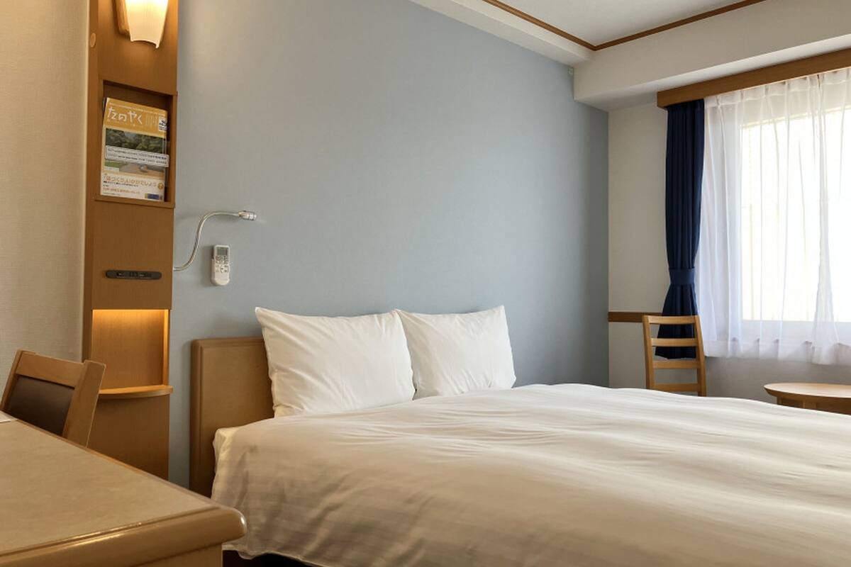Hotelkamer met een bed, bureau, stoel, nachtkastje, lamp, telefoon en raam met gordijnen.