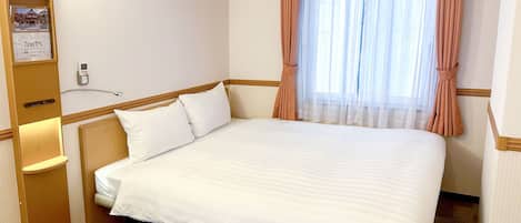 Una camera d'albergo con un letto grande, un comodino, un tavolino e un telefono fissato al muro, oltre a una finestra con tende.