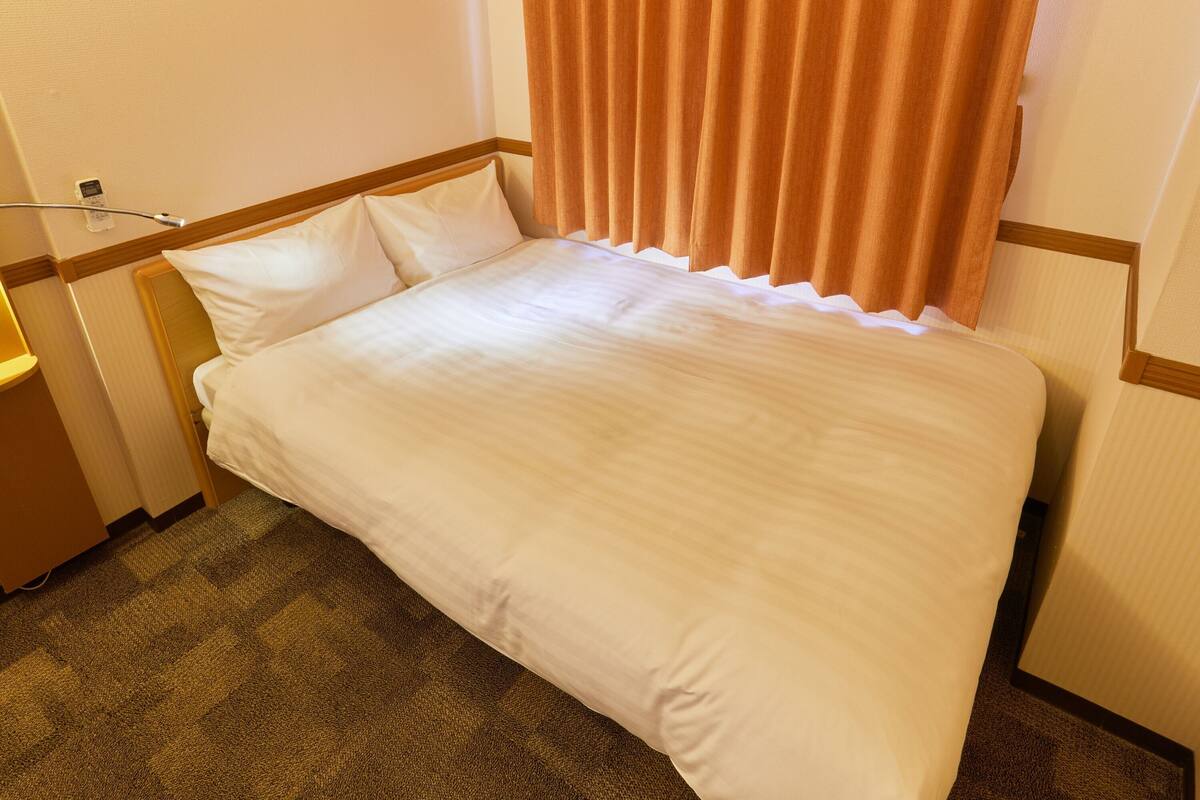 Ein Hotelzimmer mit Bett, Nachttisch, Lampe und einem fenster mit Vorhängen.