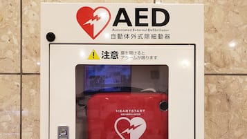 An AED (Automated External Defibrillator) box with a red heart symbol, a warning sign, and text in multiple languages.