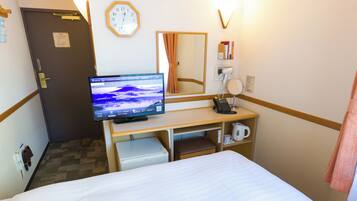 Quarto de hotel com cama, escrivaninha com monitor de computador, telefone, chaleira e relógio na parede.