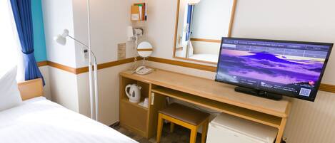 Ein Hotelzimmer mit Bett, Schreibtisch mit Computer, Spiegel, Telefon und kleinem Kühlschrank.