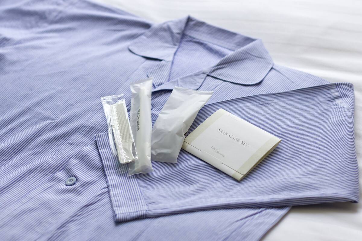A neatly folded blue shirt with a skin care set on top, including a tube, a brush, and a packet.