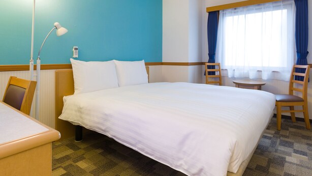 A hotel room with a large bed, a desk, a chair, a lamp, and a window with curtains. - Toyoko Inn Yokohama Stadium Mae No.2 (Yokohama)