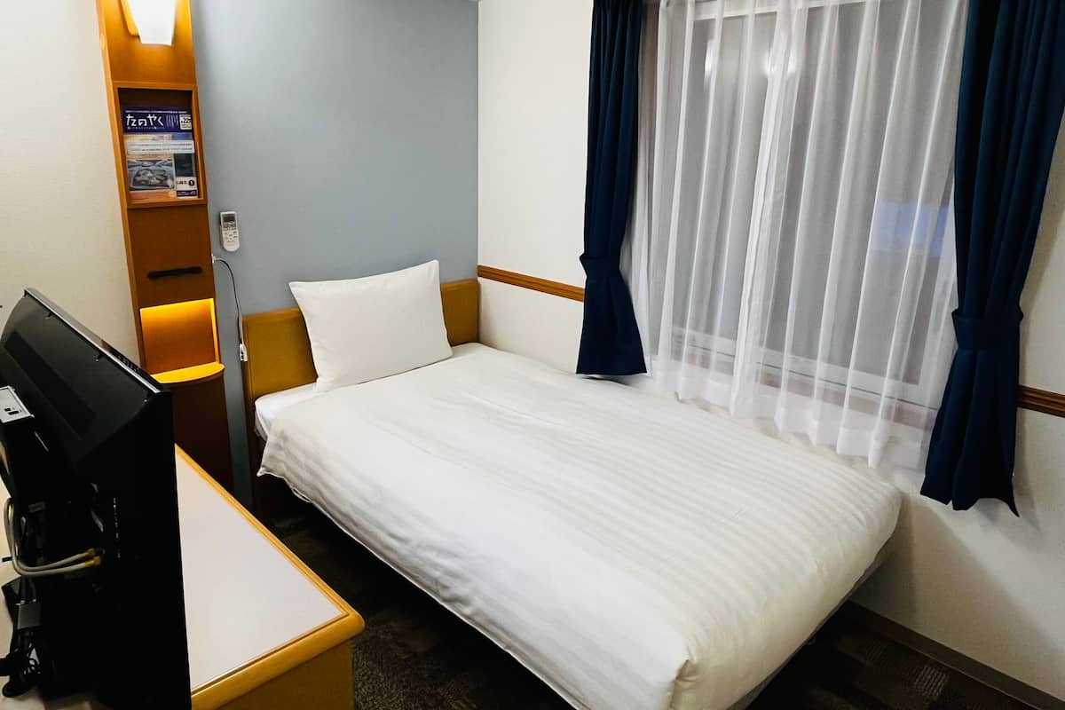 Ein Hotelzimmer mit Bett, Schreibtisch, Computer, Telefon und einem Fenster mit Vorhängen.