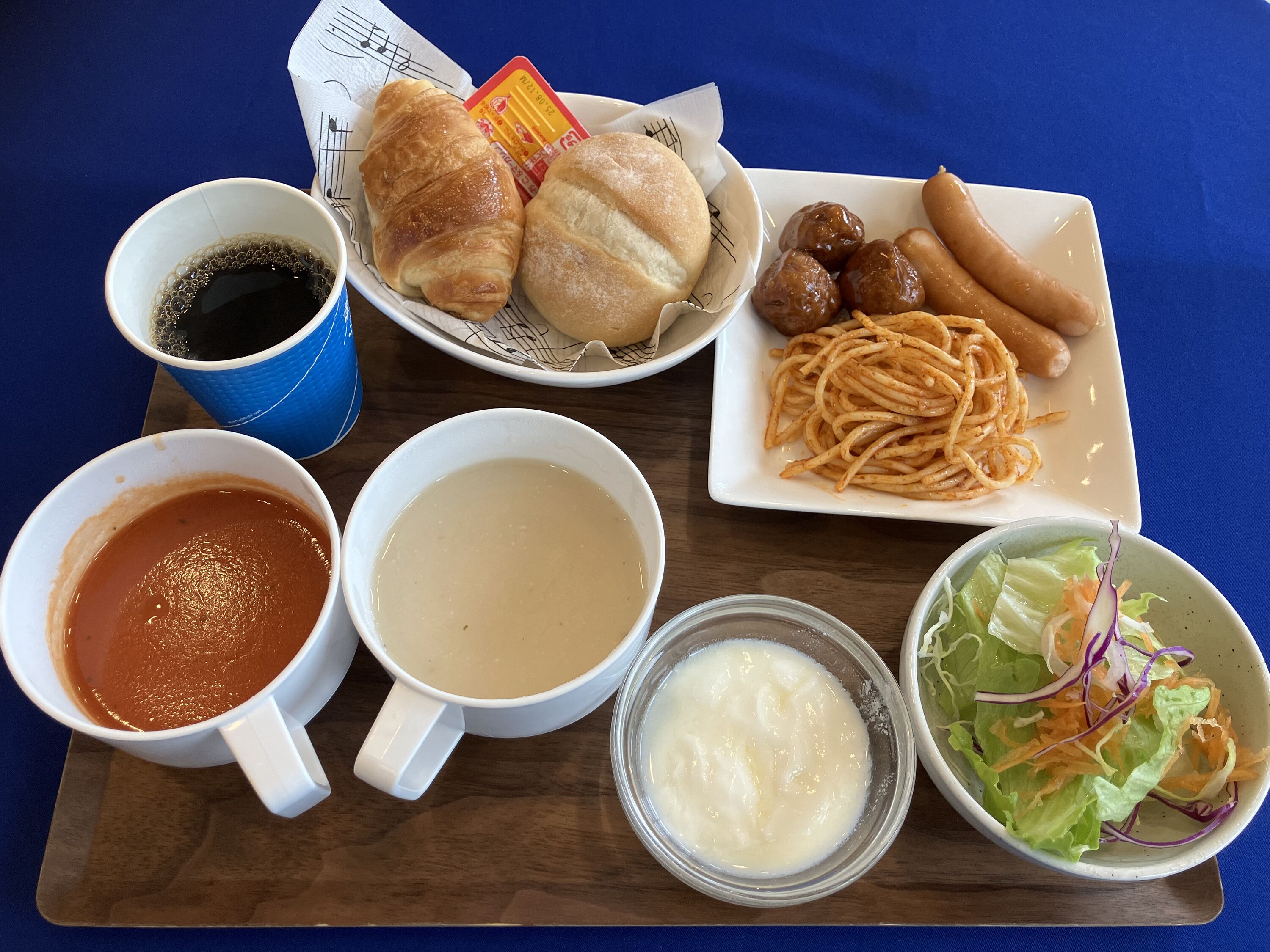 Un plateau contenant divers aliments, notamment de la soupe, des pâtes, du pain et une salade.