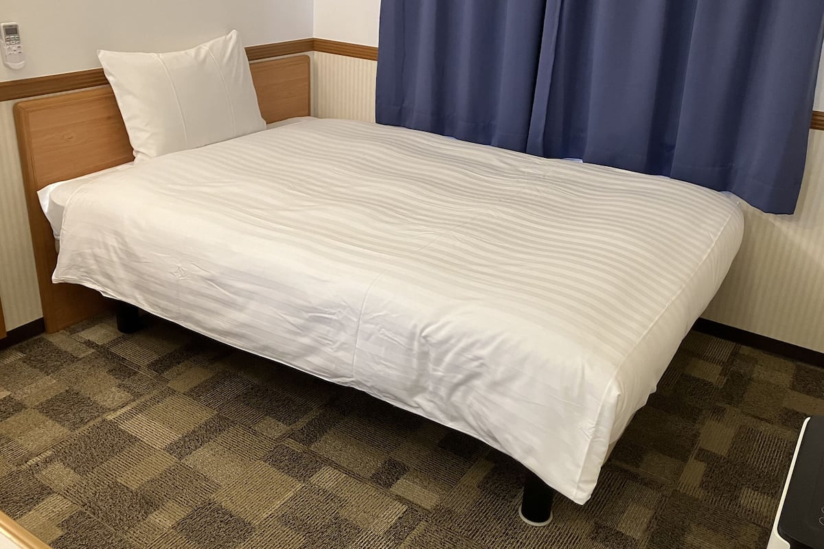 Una cama individual con cabecera de madera, ropa de cama blanca y una alfombra a cuadros.