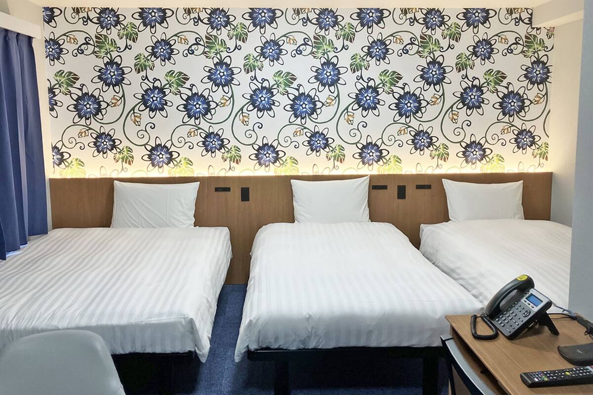 Habitación de hotel con dos camas, un escritorio con teléfono y un papel tapiz decorado con motivos florales.
