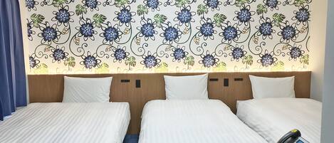 A hotel room with two beds, a desk with a telephone, and a decorative floral wallpaper.