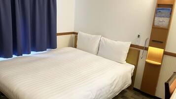 A hotel room with a large bed, a wooden headboard, a nightstand, a wall-mounted lamp, and a small shelf with a map and a phone.