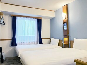 A hotel room with two beds, a large window with blue curtains, a bedside table with a lamp, and a wall-mounted TV. - Toyoko Inn Kumamoto Sakuramachi Bus Terminal Mae (Kumamoto)