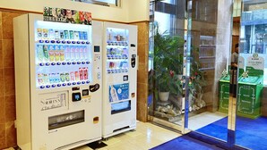 Vending machines with various products, a glass door entrance, and a potted plant inside. - Toyoko Inn Kumamoto Sakuramachi Bus Terminal Mae (Kumamoto)