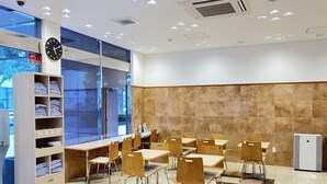 A modern indoor space with tables and chairs, a clock, and a large window. - Toyoko Inn Kumamoto Sakuramachi Bus Terminal Mae (Kumamoto)