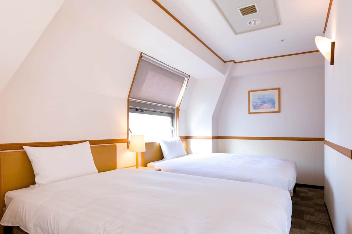 Ein Hotelzimmer mit zwei Betten, einem Fenster mit Blick, einem Gemälde an der Wand und einem Deckenlüfter.