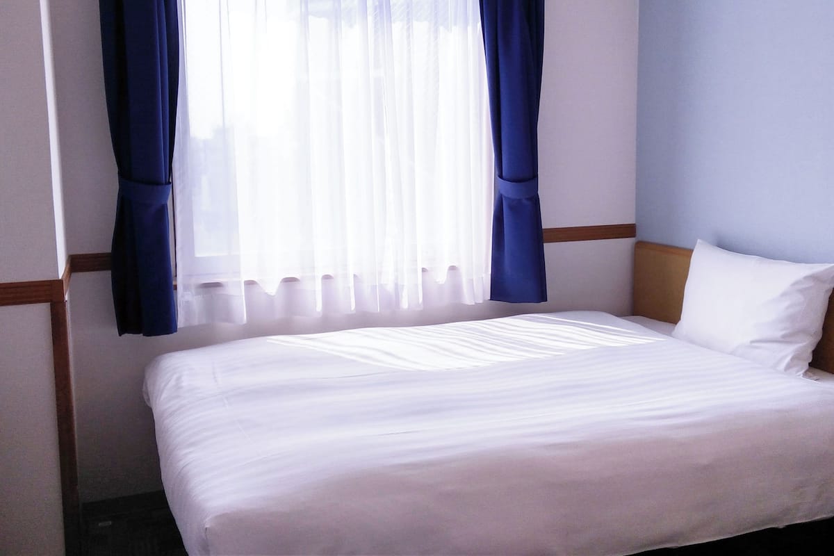 Ein Hotelzimmer mit Bett, weißen Vorhängen und einem Fenster mit transparenten weißen Vorhängen.