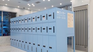 A row of blue self-service lockers with numbered keys, a sign indicating operating hours, and a ventilation system on the right. - Toyoko Inn Tokyo Shinjuku Kabukicho (Tokyo)