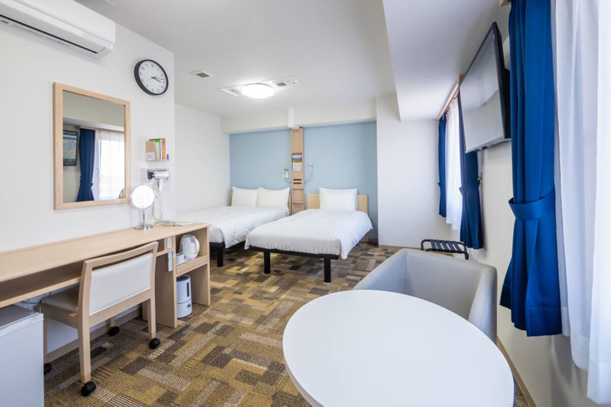 Ett hotellrum med en säng, ett skrivbord med en spegel, ett litet bord, ett badkar och ett fönster med gardiner.