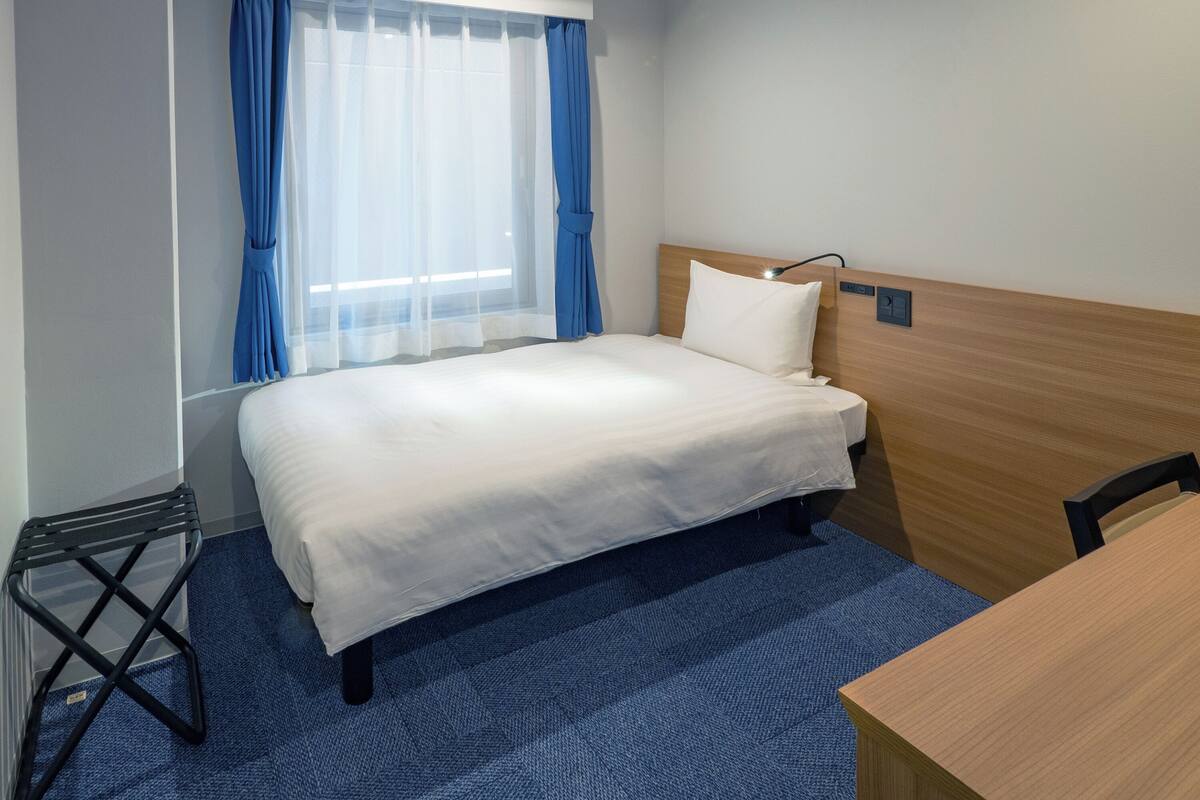 Ett hotellrum med en säng, ett skrivbord och ett fönster med blå gardiner.