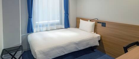 A hotel room with a bed, a desk, and a window with blue curtains.
