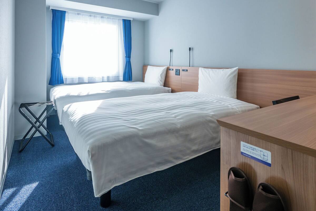 Ett hotellrum med två sängar, ett skrivbord och ett par tofflor.