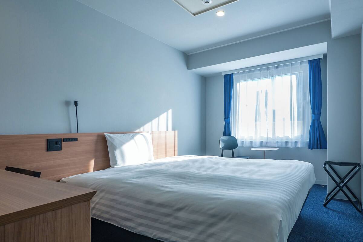Ett hotellrum med en säng, ett skrivbord, en stol och ett litet bord.