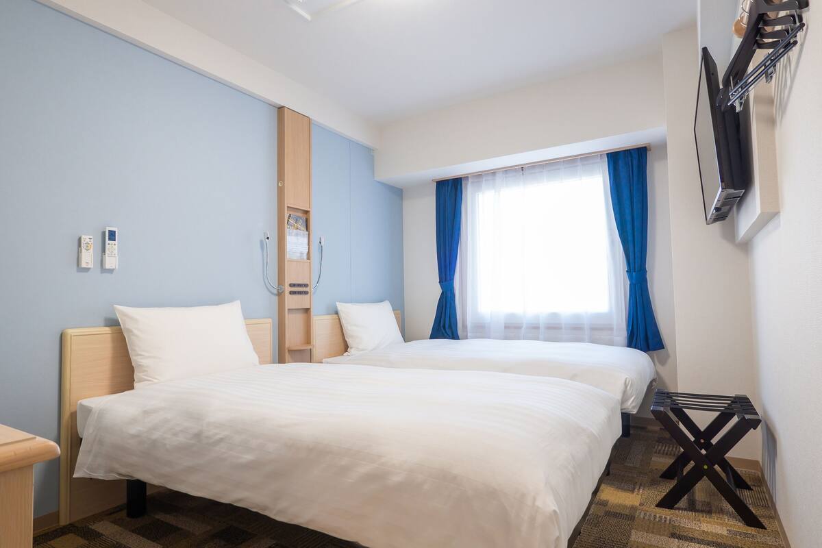 Ett hotellrum med två sängar, en TV som är monterad på väggen och ett fönster med blå gardiner.