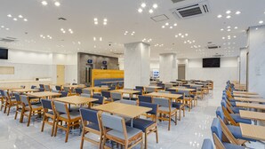 A spacious dining area with multiple tables and chairs, a counter with a cash register, and a large screen on the wall. - Toyoko Inn Nagasaki Ekimae (Nagasaki)
