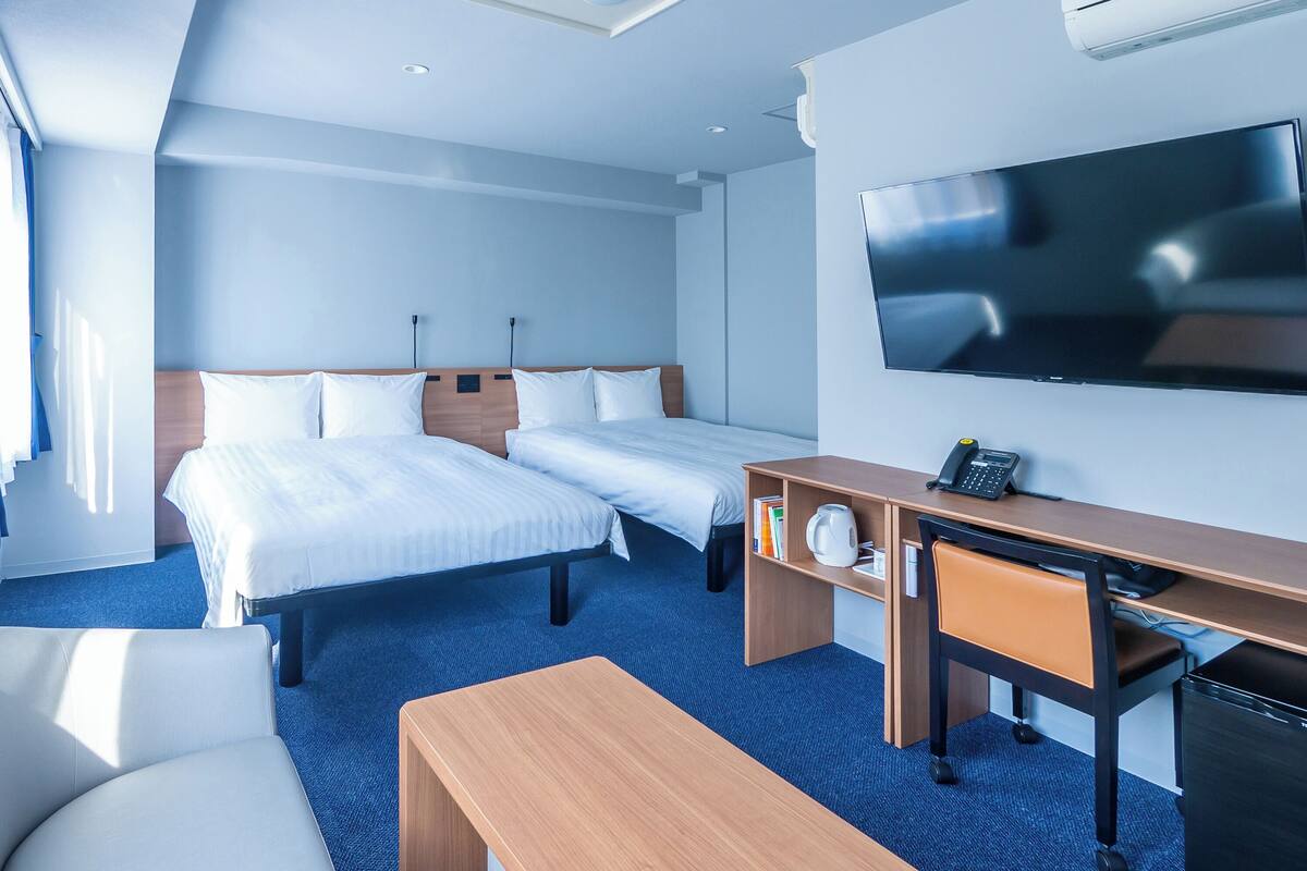 Ett hotellrum med två sängar, ett skrivbord, en stol, en TV och en luftkonditioneringsanläggning.