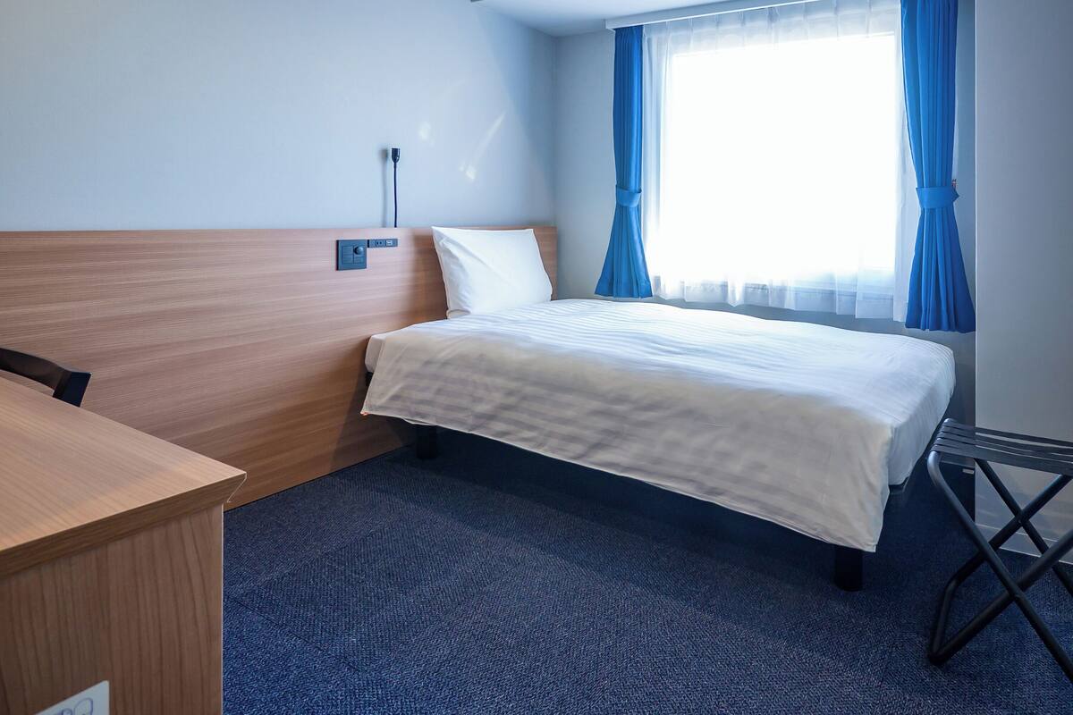 Ett hotellrum med en säng, ett skrivbord och ett fönster med gardiner.