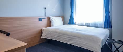 A hotel room with a bed, a desk, and a window with curtains.
