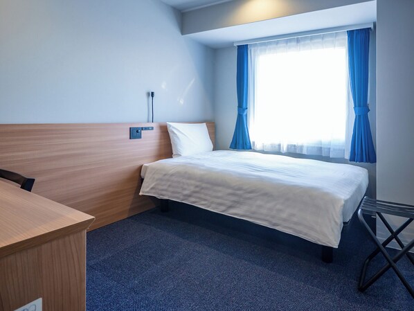 A hotel room with a bed, a desk, and a window with curtains.