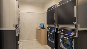 A laundry facility with multiple washing machines and dryers, a digital control panel, and a small wooden cabinet. - Toyoko Inn Nagasaki Ekimae (Nagasaki)