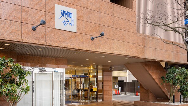 A hotel entrance with a sign indicating the name in both English and another language, a glass door entrance, and a ramp leading to the main building.
