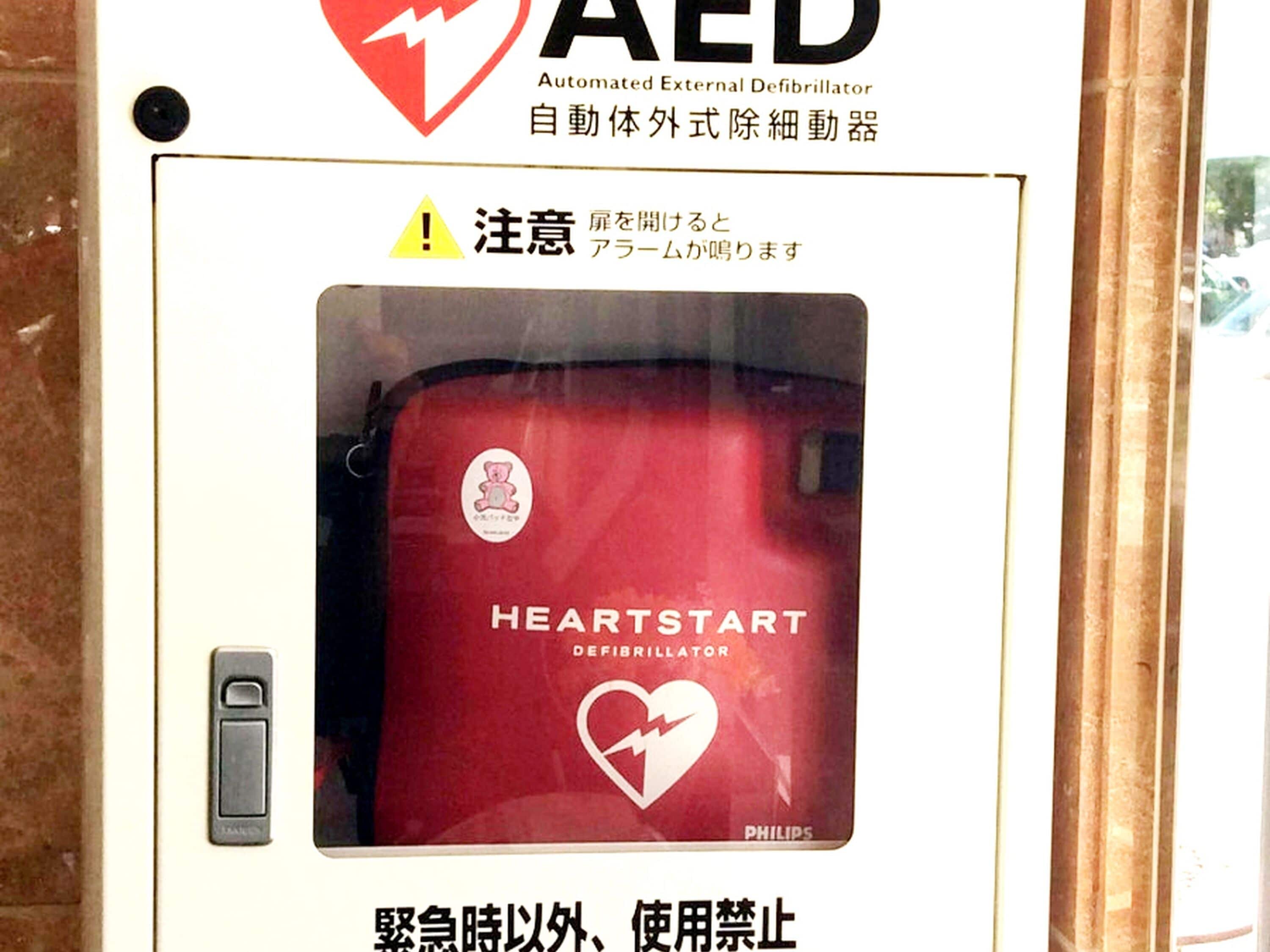Schild für einen AED (Automatisierten Externen Defibrillator) mit der Warnung, die Tür offen zu halten.